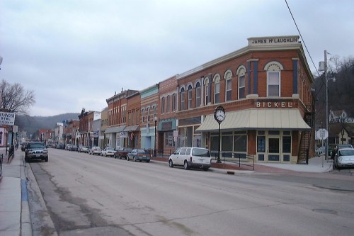 A quiet street lined with historic brick buildings and parked cars under a cloudy sky.