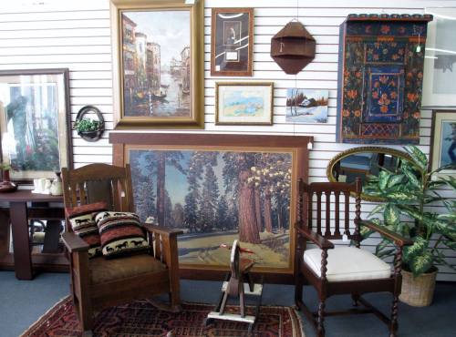 A cozy display of vintage furniture and artwork, featuring chairs, paintings, and decorative items against a wall.
