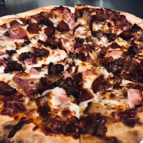 A close-up of a pizza topped with cheese, ham, sausage, and pepperoni, with a golden-brown crust.