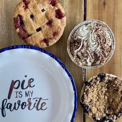 A wooden table with a pie, a dessert in a bowl, and a plate that says "Pie is my favorite."