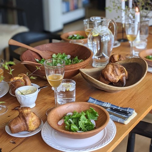 A wooden table set with bowls of salad, drinks, and golden-brown pastries, creating a cozy dining atmosphere.