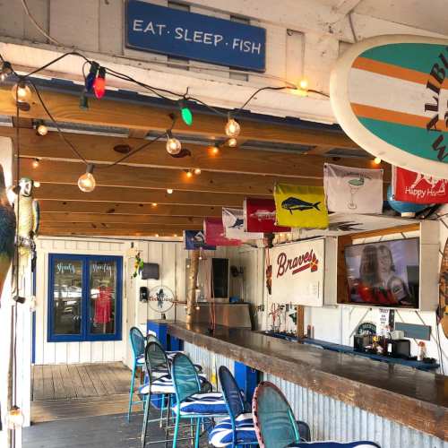 A cozy beach-themed bar with string lights, surfboards, and colorful flags, inviting patrons to relax and enjoy.