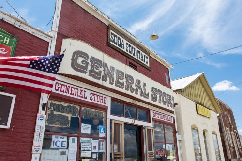 A vintage general store with a soda fountain, featuring an American flag and colorful signage under a blue sky.