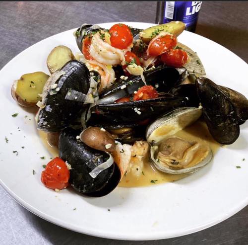 A plate of seafood featuring mussels, shrimp, clams, cherry tomatoes, and herbs in a savory broth.