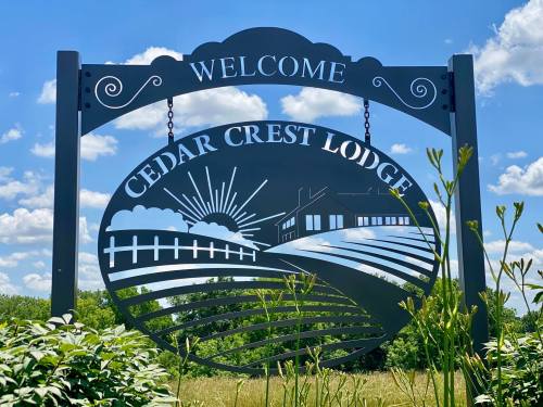 A decorative sign reading "Welcome Cedar Crest Lodge" with a sun and landscape design against a blue sky.