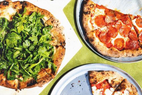 Two pizzas on metal plates: one topped with pepperoni and the other with fresh arugula, on a green table.