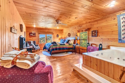Cozy wooden bedroom with a large bed, seating area, and a hot tub, featuring scenic views through large windows.