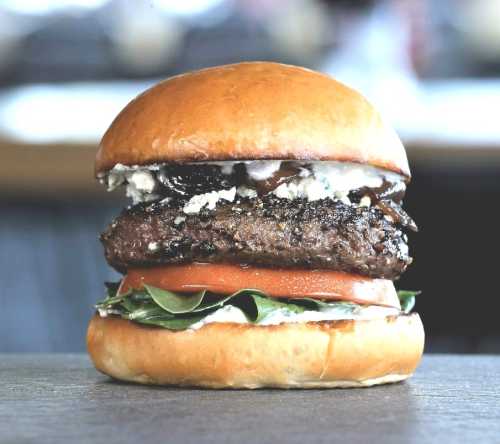 A delicious burger with a juicy patty, fresh spinach, tomato, and blue cheese, all in a toasted bun.