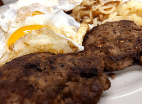 A close-up of a breakfast plate featuring two sausage patties, fried eggs, and hash browns.
