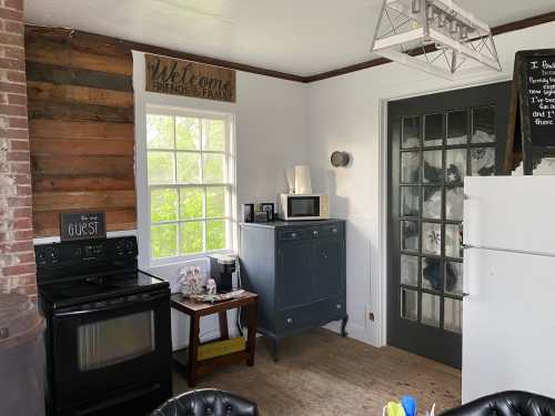 Cozy kitchen with a black stove, gray cabinet, and a welcoming sign on the wall, featuring natural light from the window.