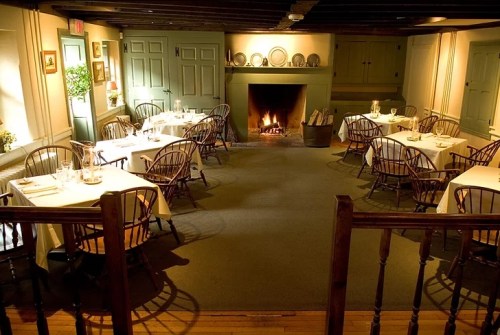 Cozy dining room with wooden tables, chairs, and a fireplace, creating a warm, inviting atmosphere.
