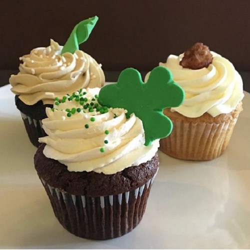 Three decorated cupcakes: one chocolate with green sprinkles, one vanilla with a green leaf, and one vanilla with a cookie on top.