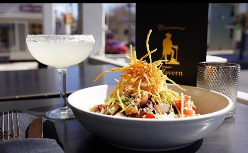 A vibrant salad topped with crispy strips, alongside a margarita in a glass with a salted rim, set on a table.