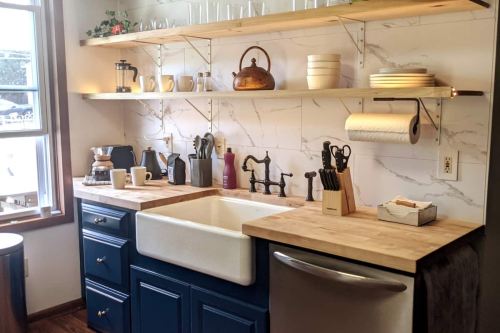 A modern kitchen with a farmhouse sink, wooden countertops, open shelves, and various kitchenware displayed.