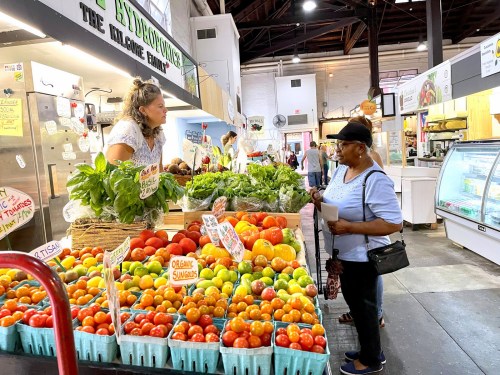 A vendor talks to a customer at a vibrant market stall filled with fresh fruits and vegetables.