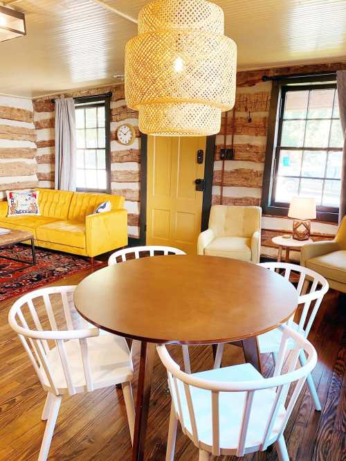 Cozy interior featuring a round table, white chairs, yellow sofa, and a large woven pendant light in a rustic setting.