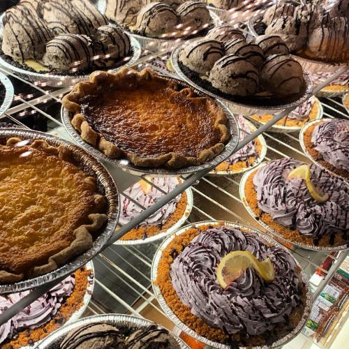 A display of various pies and desserts, including chocolate, lemon, and sweet potato, arranged on a shelf.