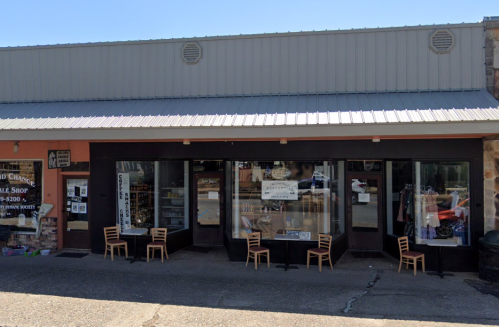 A storefront with large windows, displaying items for sale, and small chairs arranged outside on the pavement.