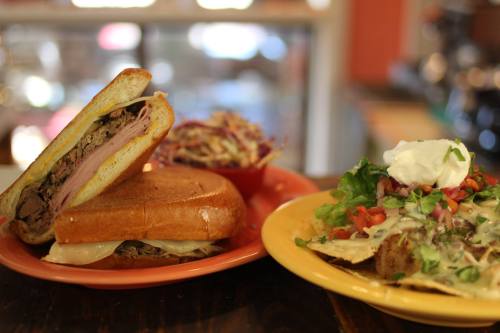 A plate with a sandwich and a side of coleslaw, alongside another plate of nachos topped with lettuce, tomatoes, and sour cream.