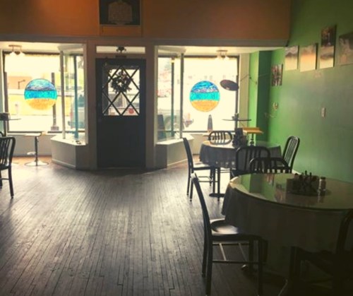 Cozy café interior with wooden floors, tables, and colorful stained glass lamps by large windows.