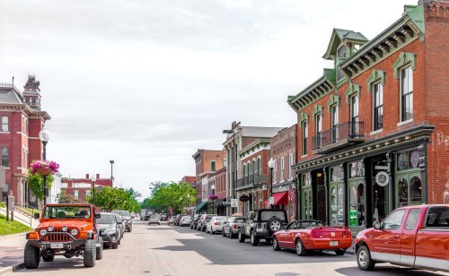 A charming street lined with historic buildings and parked cars, featuring an orange jeep in the foreground.