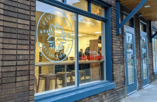 Exterior view of a bakery with large windows displaying the logo and interior seating.
