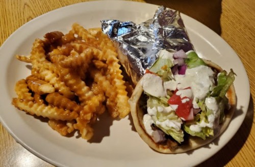 A plate with crinkle-cut fries and a foil-wrapped wrap filled with lettuce, tomatoes, and sauce.