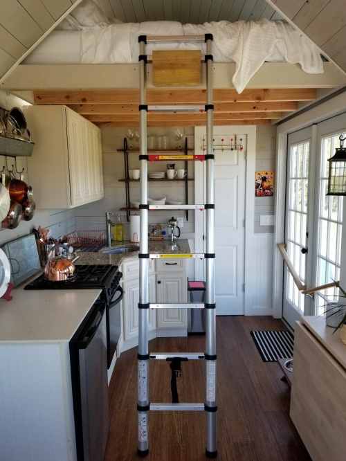 A small kitchen with a lofted bed accessed by a ladder, featuring white cabinets and a cozy, rustic design.