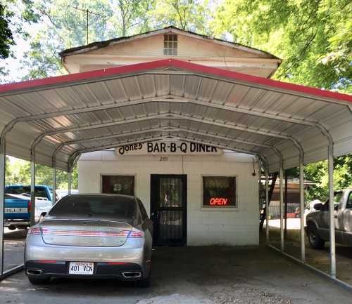 A small diner with a red awning, featuring an "Open" sign and a parked silver car in front.