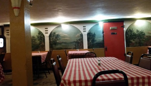 Interior of a restaurant with checkered tablecloths, murals on the walls, and a red door in the background.