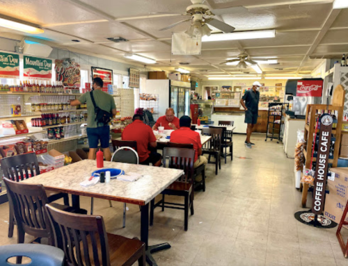 A cozy café interior with tables, patrons dining, and shelves stocked with snacks and drinks.