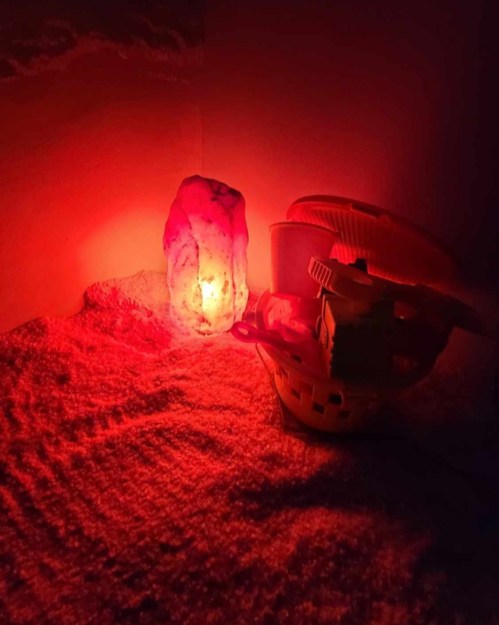 A glowing red salt lamp beside a white basket on a textured surface, creating a warm, ambient light.