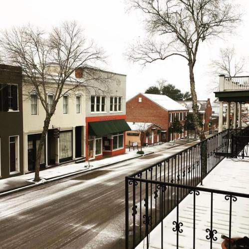 A snowy street scene with bare trees, quaint buildings, and a quiet atmosphere.