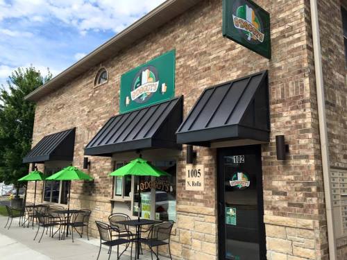 Exterior of a brick building with green accents, featuring outdoor seating and a sign for "Pudge's."