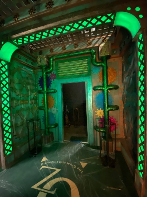 A brightly lit entrance with green pipes and decorative gears, set in a colorful, themed environment.