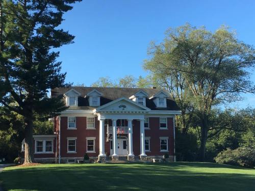 A large red brick house with white columns, surrounded by trees and a green lawn under a clear blue sky.