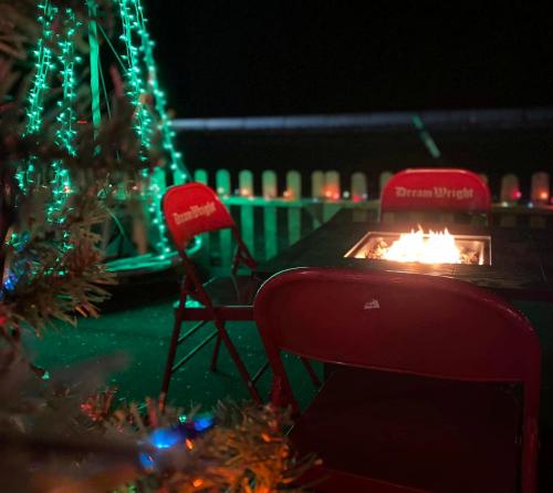 A cozy outdoor setting with red chairs, a fire pit, and festive green lights in the background.