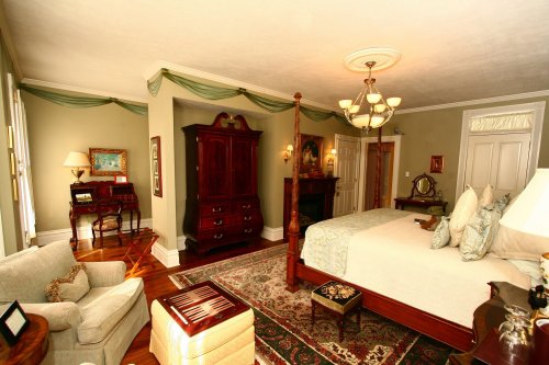 A spacious, elegantly decorated bedroom featuring a four-poster bed, antique furniture, and soft lighting.