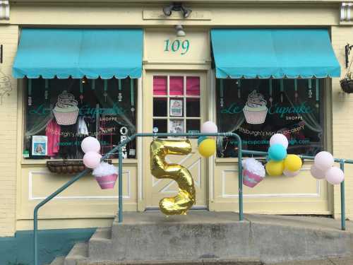 A colorful storefront with a "5" balloon and cupcake decorations, celebrating an event at Le Cupcake Shoppe.