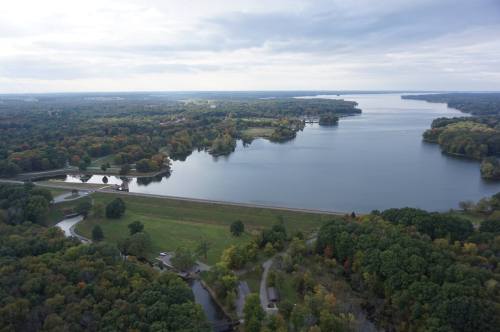 Aerial view of a serene lake surrounded by lush greenery and trees, with a cloudy sky above.