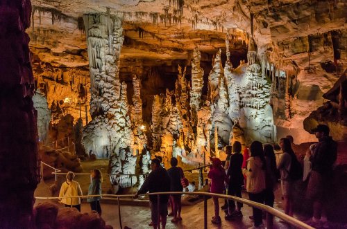 Visitors explore a stunning cave filled with stalactites and stalagmites, illuminated by warm lighting.
