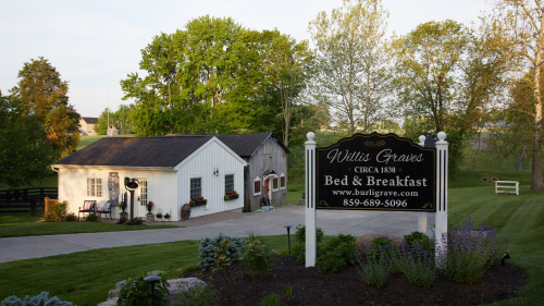 A charming bed and breakfast sign in front of a white building, surrounded by lush greenery and blooming flowers.