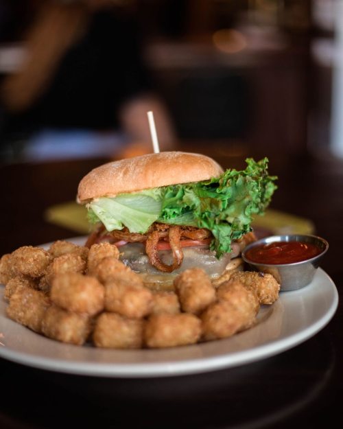 A juicy burger topped with lettuce and bacon, served with a side of crispy tater tots and ketchup.