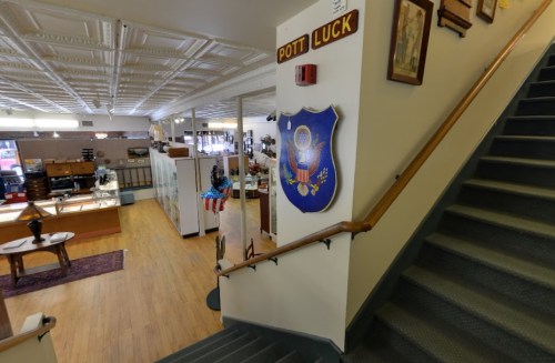 Interior of a store with a staircase, featuring a "Pott Luck" sign and a U.S. emblem on the wall.