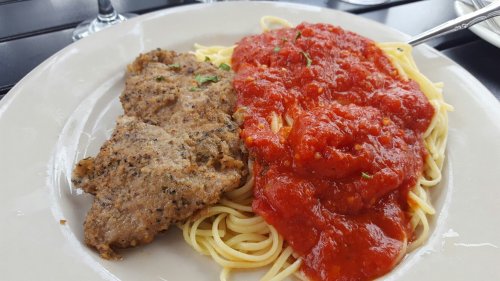 A plate of spaghetti topped with marinara sauce, alongside a piece of seasoned meat.