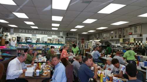 A busy diner with patrons enjoying meals at tables, surrounded by shelves of products and a prescription counter.