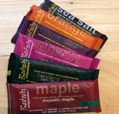 A variety of chocolate bars in colorful wrappers: sea salt, orange, black raspberry, cherry, espresso, and maple.