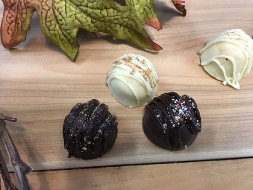 Four assorted chocolate truffles on a wooden surface, featuring dark and white chocolate with decorative toppings.