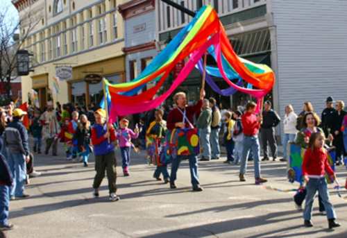 A colorful parade with people holding banners and ribbons, celebrating in a lively street scene.