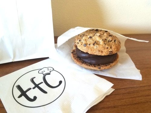 A chocolate-covered cookie sandwich on a napkin, next to a branded paper bag with a logo.